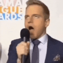 a man in a suit and tie is standing in front of a microphone .