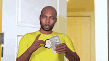 a man in a yellow shirt holds a stack of 20 dollar bills