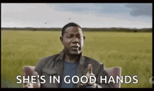 a man is sitting in a chair with his hands out in front of a field and says `` she 's in good hands '' .