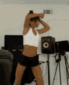 a woman in a white tank top and black shorts is dancing in a room .