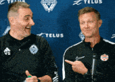 two men laughing in front of a telus banner
