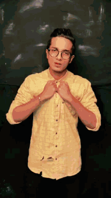 a young man wearing glasses and a yellow shirt adjusts his shirt
