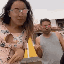 a man and a woman wearing sunglasses are standing next to each other in front of a yellow house .