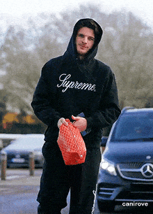 a man wearing a supreme hoodie holds a bag