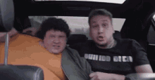 two fat men are sitting in the back seat of a car .