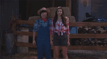 a man in a cowboy hat and overalls stands next to a woman in a plaid shirt