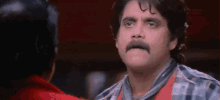 a man with a mustache is talking to another man in a red shirt .
