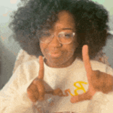 a woman with curly hair and glasses is wearing a mcdonald 's shirt and making a peace sign with her hands .