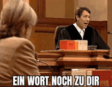 a man in a judge 's robe is sitting at a podium in front of a woman in a courtroom .