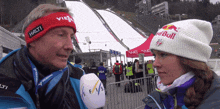 a man wearing a red halti headband is talking to a woman wearing a white red bull hat