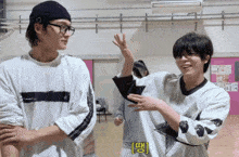 two young men are standing next to each other with one wearing glasses and the other wearing a black beanie