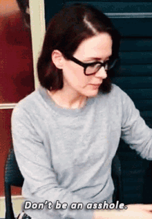 a woman wearing glasses and a grey sweater says don 't be an asshole