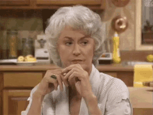 an elderly woman with gray hair is sitting at a table in a kitchen .