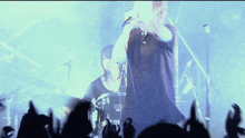 a man sings into a microphone while a woman plays drums in the background