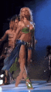 a woman in a green top and blue skirt is dancing on stage