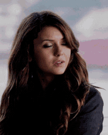 a woman with long brown hair is wearing a black jacket and has her eyes closed .