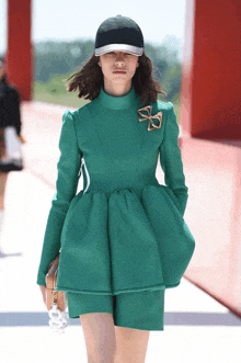 a woman wearing a green dress and a black hat is walking down a runway