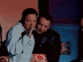 a woman singing into a microphone next to a man holding a book that has the letter q on it