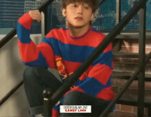 a man wearing a red and blue striped sweater sits on stairs