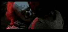 a clown with red hair is holding a woman 's hand in a dark room .