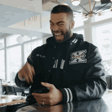 a man wearing a black jacket with the letter x on it is laughing