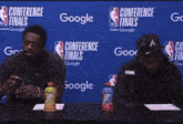 two men sit at a table in front of a conference finals sign