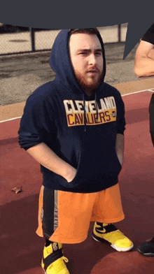 a man wearing a cleveland cavaliers hoodie stands on a basketball court