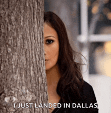 a woman peeking out from behind a tree with the words " i just landed in dallas " below her