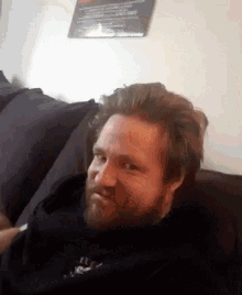 a man with a beard is sitting on a couch and making a funny face