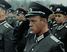 a man in a military uniform salutes in a line with other men
