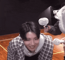 a man in a plaid shirt is smiling while someone holds a small fan over his head