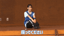 a girl in a blue shirt sits on the floor in front of a wall with chinese writing