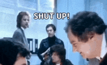 a group of men are standing around a table and talking to each other in a room .