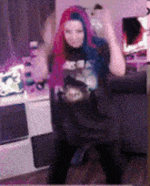 a woman with pink hair and blue eyes is sitting in a chair .