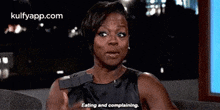 a woman in a black dress is sitting on a couch and saying `` eating and complaining '' .