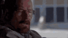 a man with glasses is sitting in a chair with his eyes closed and a beard .