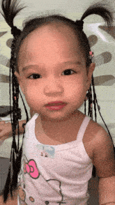 a little girl wearing a hello kitty tank top has pigtails in her hair