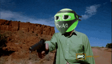 a man in a green shirt is pointing a gun with a mask that says twag on it