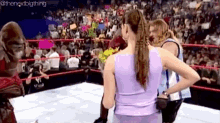 a woman in a purple top is standing in a wrestling ring with a crowd watching .