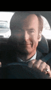 a man in a suit and tie is smiling while driving