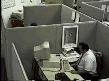 a man sits at a desk in an office cubicle with a computer