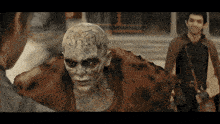 a man in a cape is standing next to a monster with a tattoo on his head