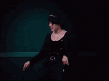 a man in a black hat and a pearl necklace is dancing in a dark room .