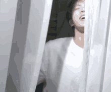 a man in a white shirt is standing in front of a white curtain and laughing .