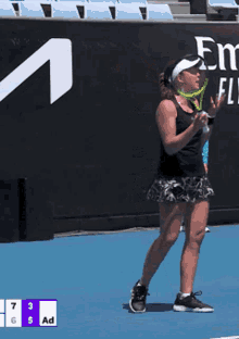 a woman holding a tennis racquet on a tennis court with emirates fly emirates written on the wall behind her
