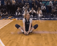 a woman sits on a basketball court with her legs crossed and a crowd watching