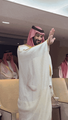 a man in a white robe and a red and white checkered head scarf is waving his hand