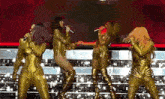 a group of women in gold outfits are singing into microphones on stage .