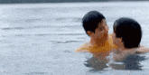 two young men are swimming in a lake together .