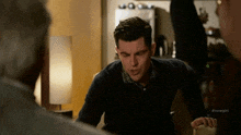 a man is sitting on a couch in a living room talking to two other men .